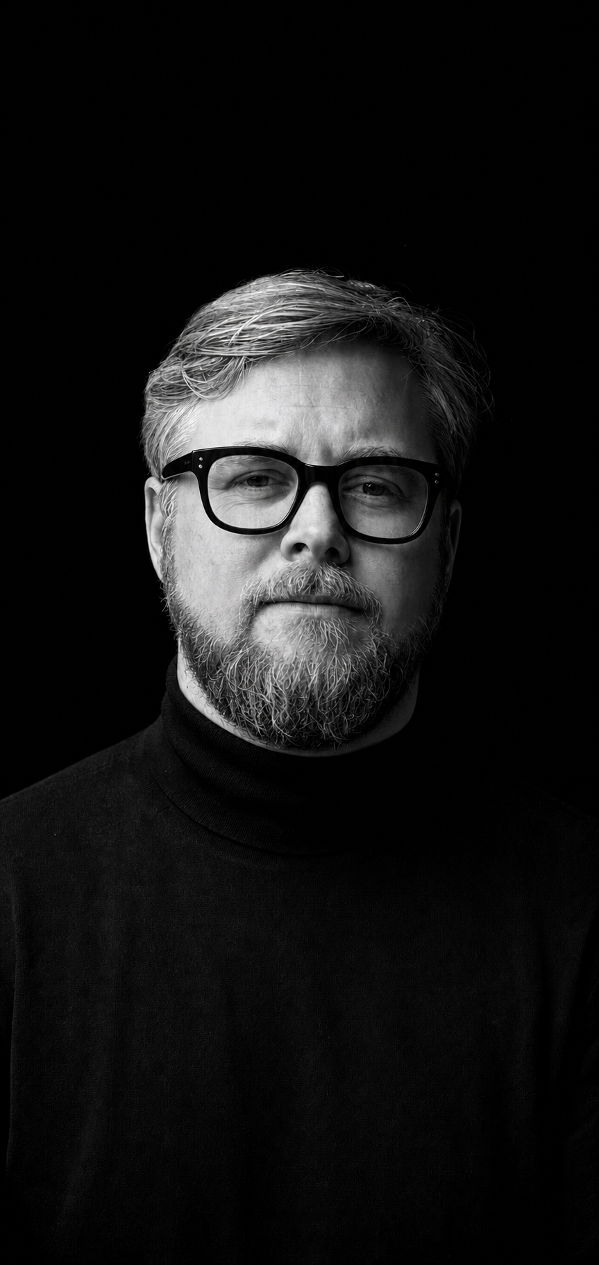 Black-and-white studio portrait of James Pendergrast wearing a black turtleneck and heavy black glasses